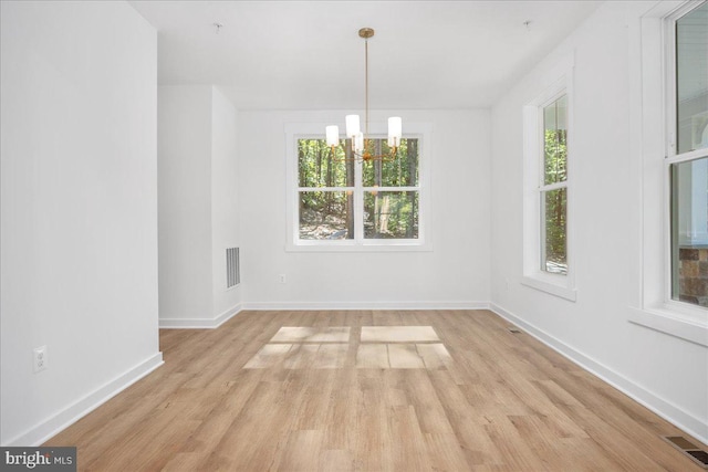 unfurnished dining area with an inviting chandelier and light wood-type flooring