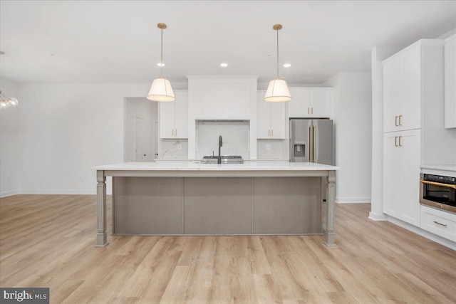 kitchen featuring appliances with stainless steel finishes, an island with sink, light hardwood / wood-style floors, and pendant lighting