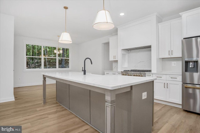 kitchen featuring stainless steel fridge with ice dispenser, an island with sink, decorative light fixtures, light stone countertops, and white cabinets