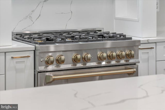 details featuring white cabinets, high end stainless steel range, and light stone counters