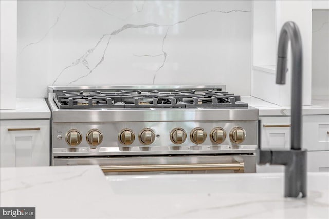 room details with white cabinetry, light stone counters, tasteful backsplash, and high end stove