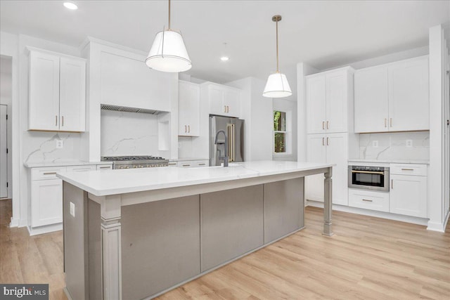 kitchen with hanging light fixtures, white cabinets, backsplash, and a center island with sink