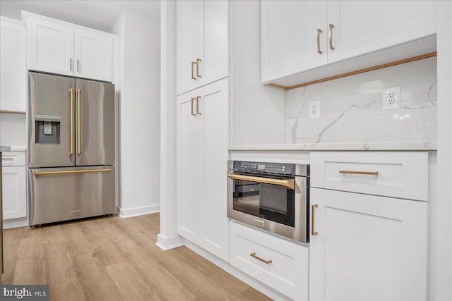 kitchen featuring tasteful backsplash, light wood-type flooring, appliances with stainless steel finishes, white cabinets, and light stone counters