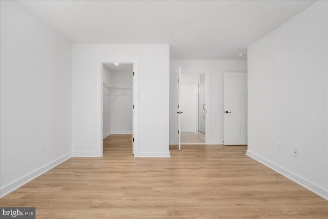 unfurnished bedroom with a walk in closet, a closet, and light hardwood / wood-style flooring