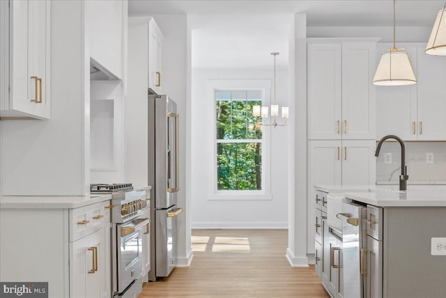 kitchen with hanging light fixtures, white cabinets, premium appliances, and light hardwood / wood-style flooring