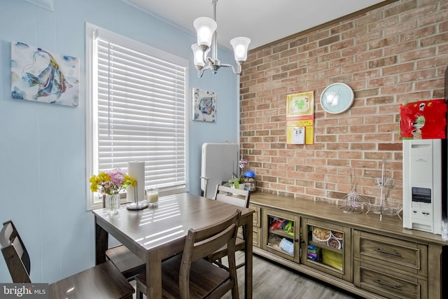 dining area with brick wall, a notable chandelier, and light wood-type flooring