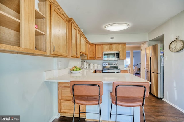 kitchen with sink, kitchen peninsula, a breakfast bar area, stainless steel appliances, and dark hardwood / wood-style floors