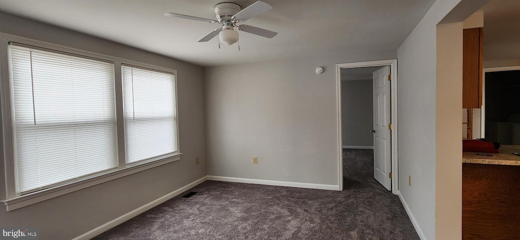 empty room featuring ceiling fan and dark carpet