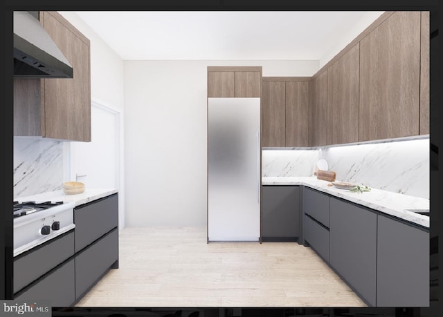 kitchen featuring tasteful backsplash, wall chimney range hood, gray cabinets, white gas cooktop, and light brown cabinetry