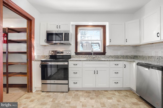 kitchen featuring appliances with stainless steel finishes, sink, light stone counters, and white cabinetry