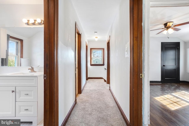 hallway with light carpet, vaulted ceiling, and sink