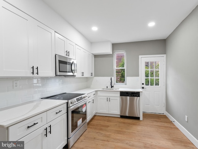 kitchen with stainless steel appliances, decorative backsplash, white cabinets, light hardwood / wood-style flooring, and sink