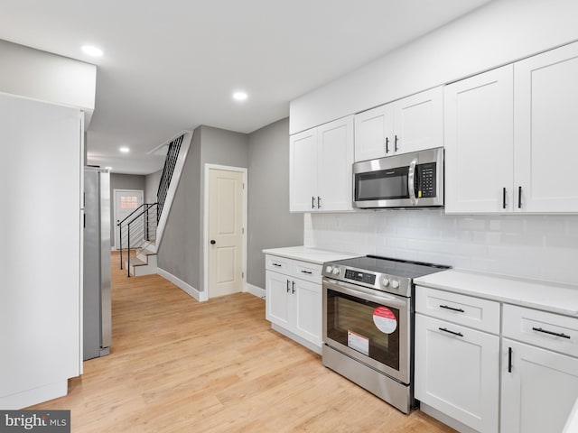 kitchen featuring appliances with stainless steel finishes, light hardwood / wood-style floors, white cabinetry, and tasteful backsplash