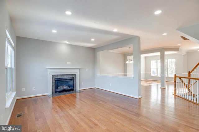 unfurnished living room featuring ornamental molding, a premium fireplace, a chandelier, and light hardwood / wood-style floors