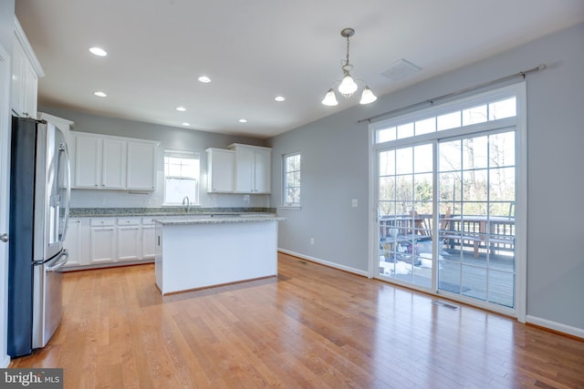 kitchen with white cabinetry, hanging light fixtures, stainless steel fridge, a kitchen island, and a healthy amount of sunlight