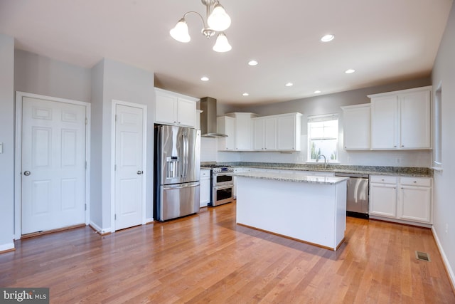 kitchen with stainless steel appliances, wall chimney range hood, and white cabinets