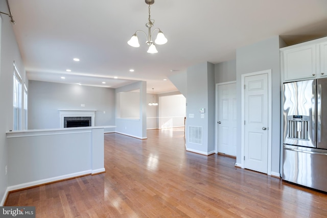 interior space with stainless steel refrigerator with ice dispenser, decorative light fixtures, a notable chandelier, hardwood / wood-style flooring, and white cabinets