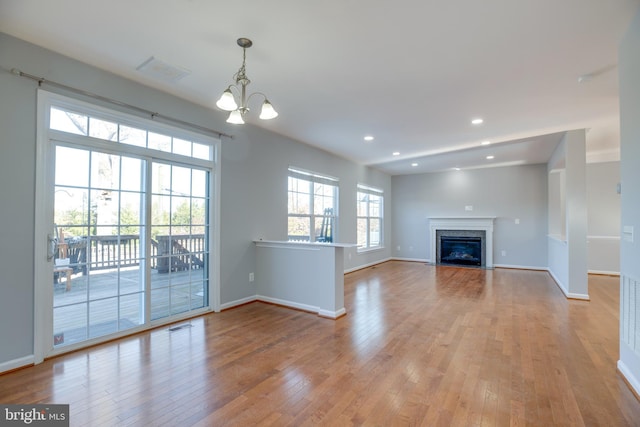 unfurnished living room featuring an inviting chandelier and light hardwood / wood-style floors