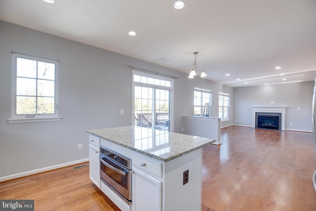 kitchen featuring stainless steel oven, decorative light fixtures, a kitchen island, and white cabinets