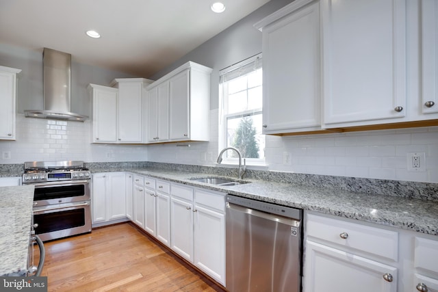 kitchen featuring wall chimney exhaust hood, sink, white cabinetry, appliances with stainless steel finishes, and light stone countertops