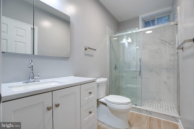 bathroom featuring a shower with door, vanity, and toilet