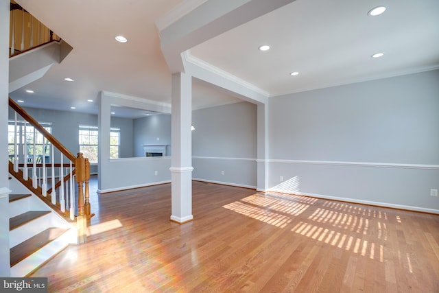 unfurnished living room with hardwood / wood-style flooring, crown molding, and decorative columns