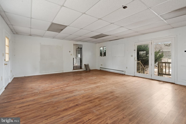 empty room featuring a paneled ceiling, a healthy amount of sunlight, and a baseboard heating unit