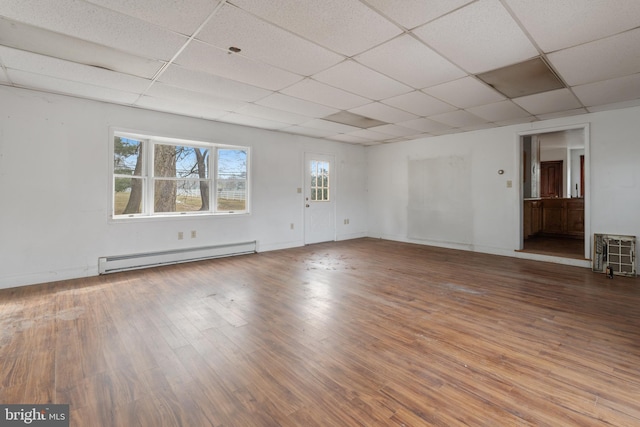 empty room featuring wood-type flooring, a drop ceiling, and a baseboard heating unit