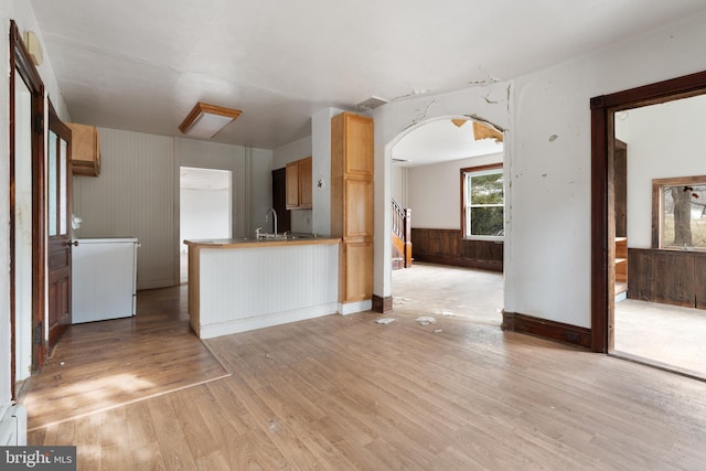 kitchen with kitchen peninsula, light brown cabinets, sink, wood walls, and light hardwood / wood-style floors