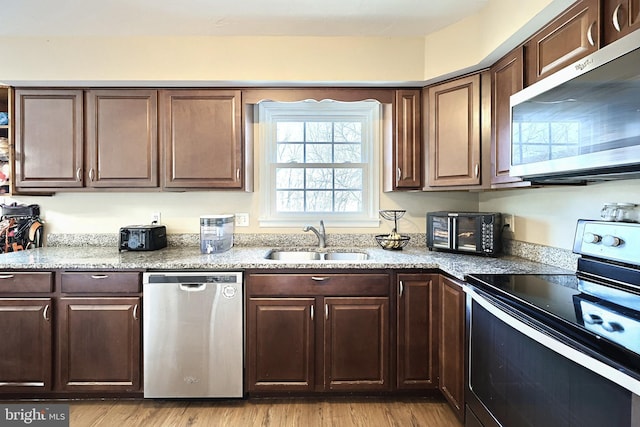 kitchen featuring sink, dark brown cabinets, appliances with stainless steel finishes, light stone countertops, and light hardwood / wood-style floors