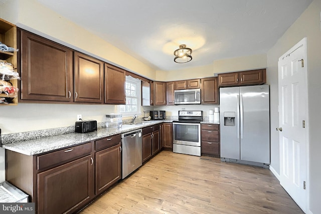 kitchen with light stone counters, appliances with stainless steel finishes, sink, and light hardwood / wood-style floors