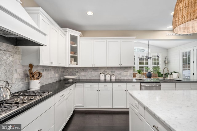 kitchen featuring premium range hood, sink, dark stone countertops, hanging light fixtures, and stainless steel appliances