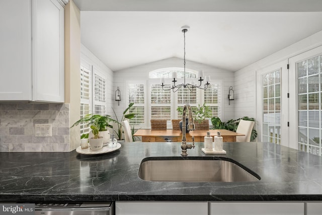 kitchen featuring pendant lighting, lofted ceiling, sink, white cabinets, and backsplash