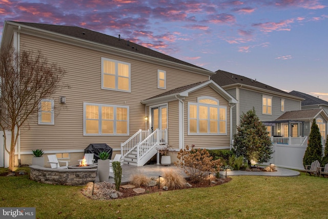 back house at dusk featuring a lawn, a patio area, and an outdoor fire pit