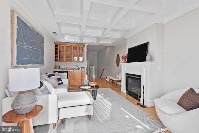 living room featuring indoor bar, beam ceiling, ornamental molding, coffered ceiling, and light hardwood / wood-style floors