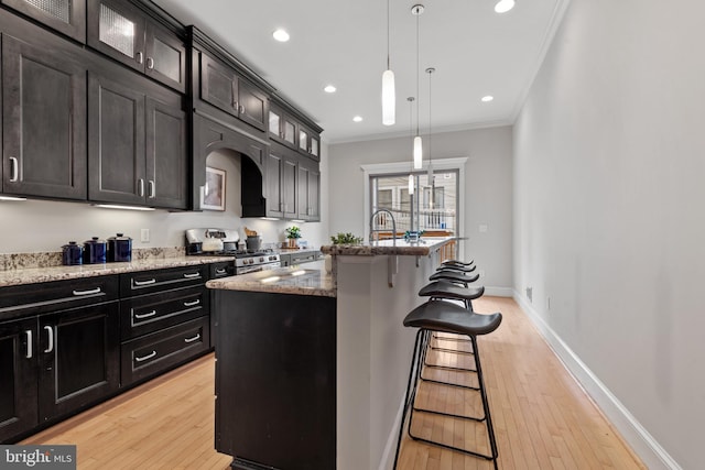 kitchen featuring a kitchen breakfast bar, hanging light fixtures, a center island with sink, crown molding, and stainless steel range with gas stovetop