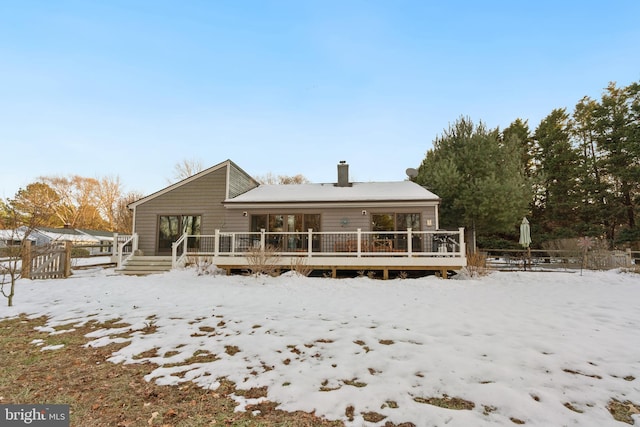 snow covered back of property with a wooden deck