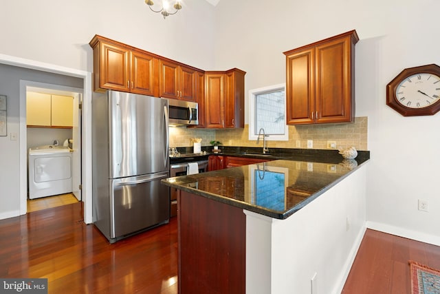 kitchen with washer / dryer, tasteful backsplash, sink, dark stone countertops, and stainless steel appliances