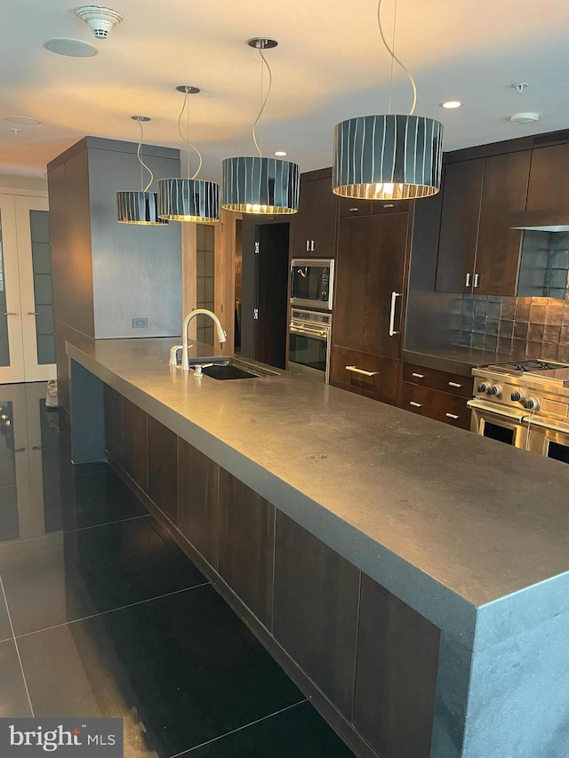 kitchen featuring appliances with stainless steel finishes, dark brown cabinets, dark tile patterned flooring, a kitchen island, and sink