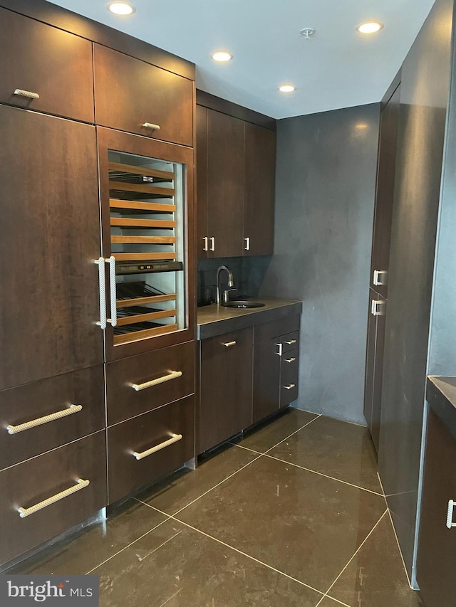 bar featuring dark tile patterned flooring, sink, and dark brown cabinets