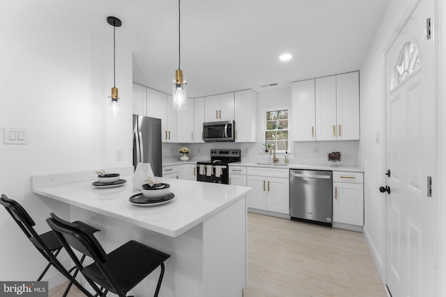 kitchen with pendant lighting, kitchen peninsula, sink, appliances with stainless steel finishes, and white cabinets