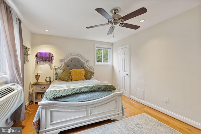 bedroom featuring a wall unit AC, ceiling fan, and light hardwood / wood-style flooring