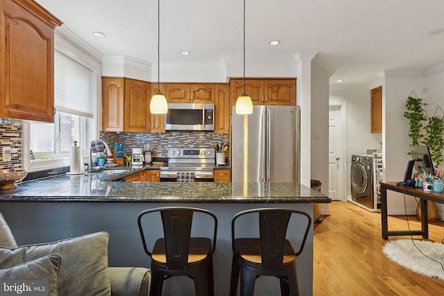 kitchen with pendant lighting, appliances with stainless steel finishes, washer / dryer, sink, and ornamental molding