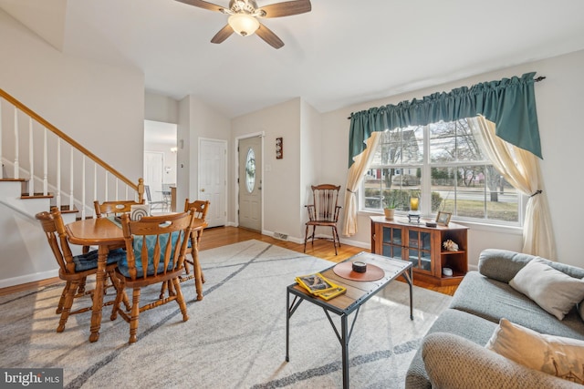 living area featuring visible vents, stairway, light wood-style flooring, a ceiling fan, and baseboards