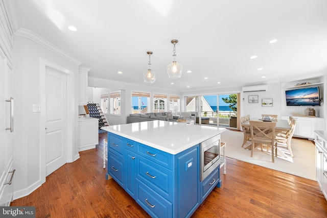 kitchen featuring white cabinetry, stainless steel microwave, blue cabinetry, a wall mounted air conditioner, and pendant lighting