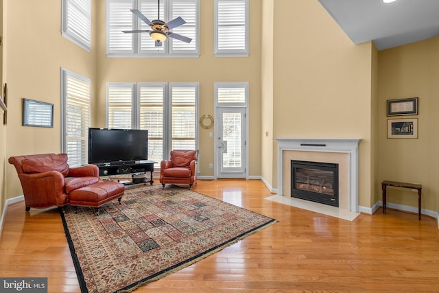 living room featuring light hardwood / wood-style floors, a premium fireplace, a high ceiling, and ceiling fan