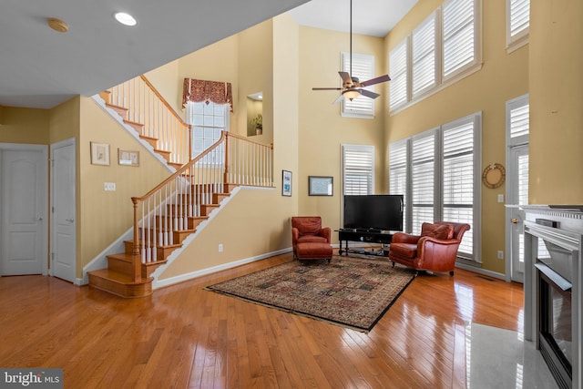 living room featuring ceiling fan, plenty of natural light, light hardwood / wood-style floors, and a high ceiling