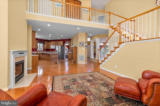 living room with a fireplace, light hardwood / wood-style floors, and a towering ceiling