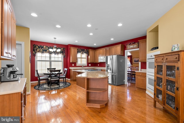 kitchen with white appliances, decorative light fixtures, light hardwood / wood-style floors, a chandelier, and a center island