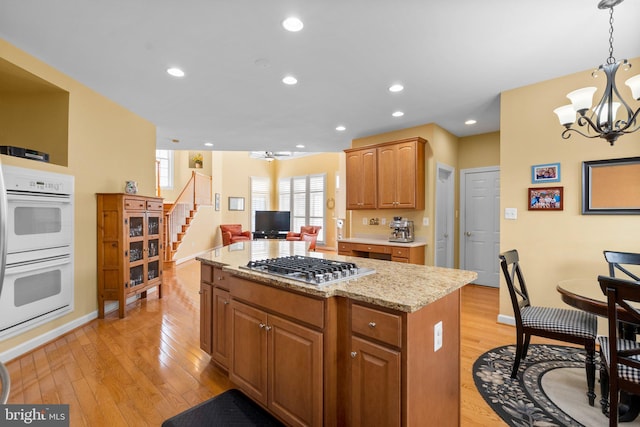 kitchen featuring stainless steel gas cooktop, hanging light fixtures, a kitchen island, light hardwood / wood-style floors, and white double oven